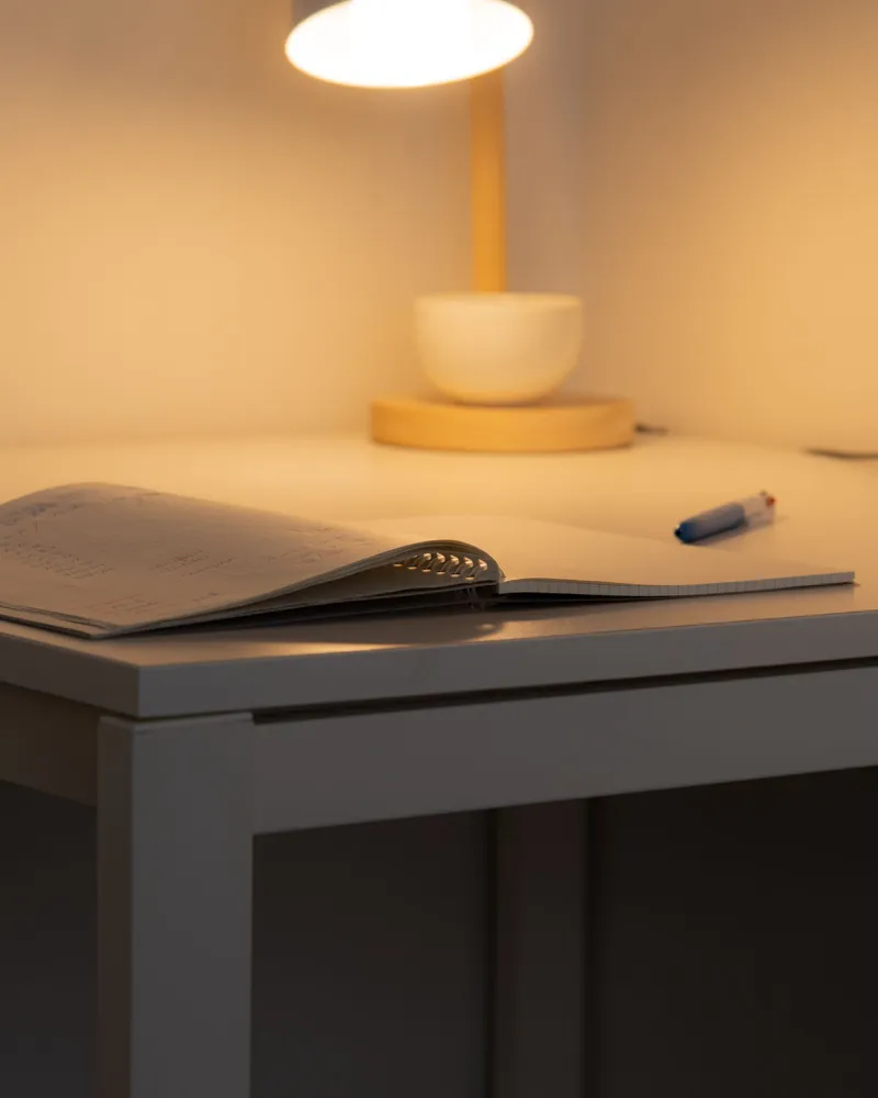 An open notebook and pen on a desk, under the warm light of a lamp