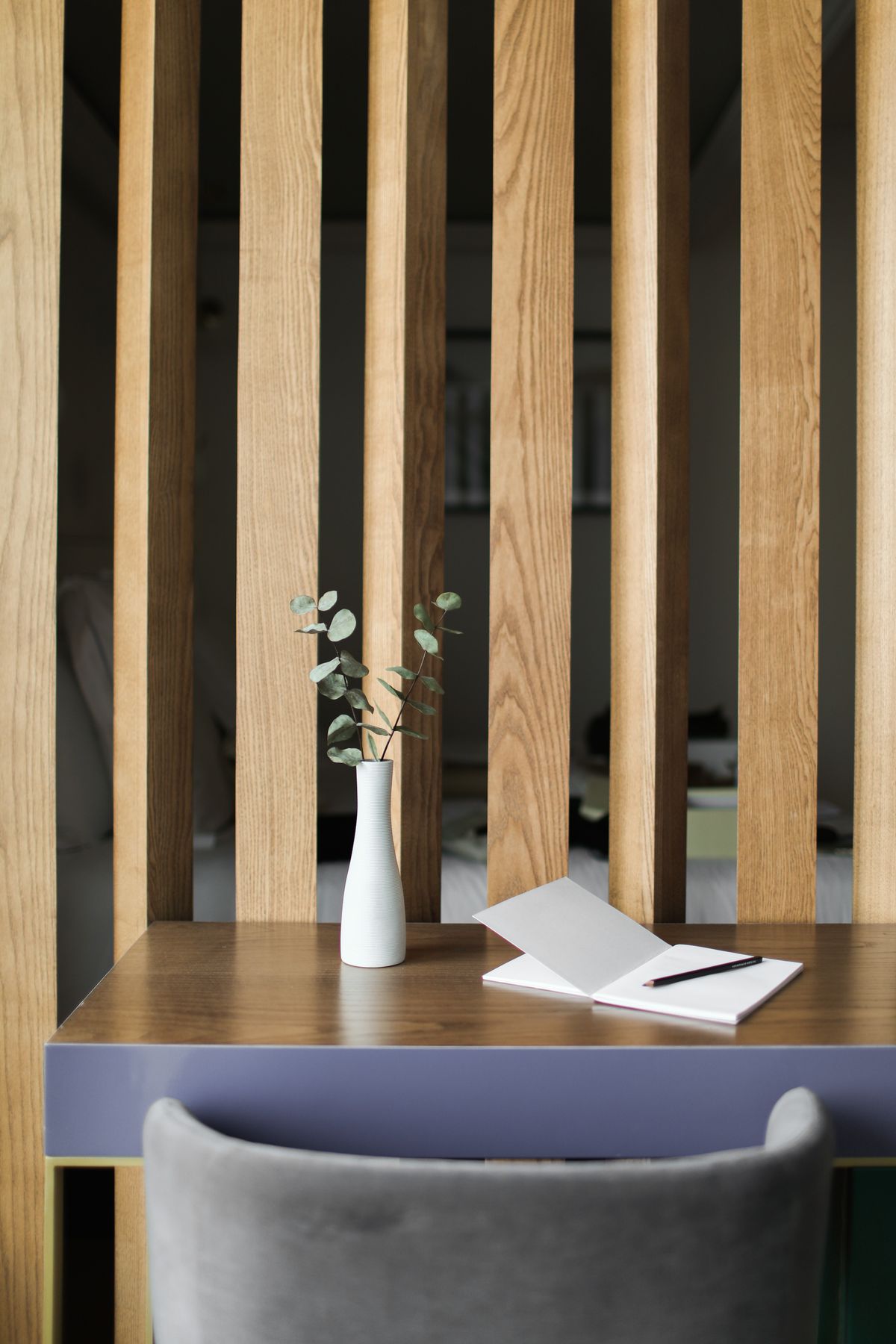 Un carnet ouvert et un crayon posés sur un bureau en bois, à côté d'un vase